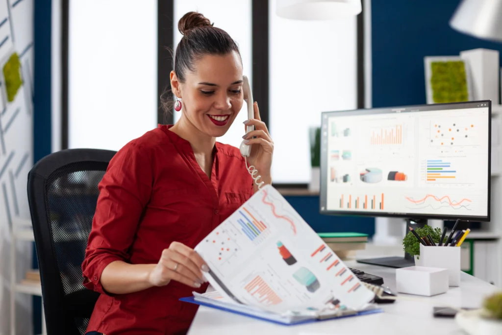 Mulher formada em Gestão Financeira EaD analisando gráficos e falando ao telefone.