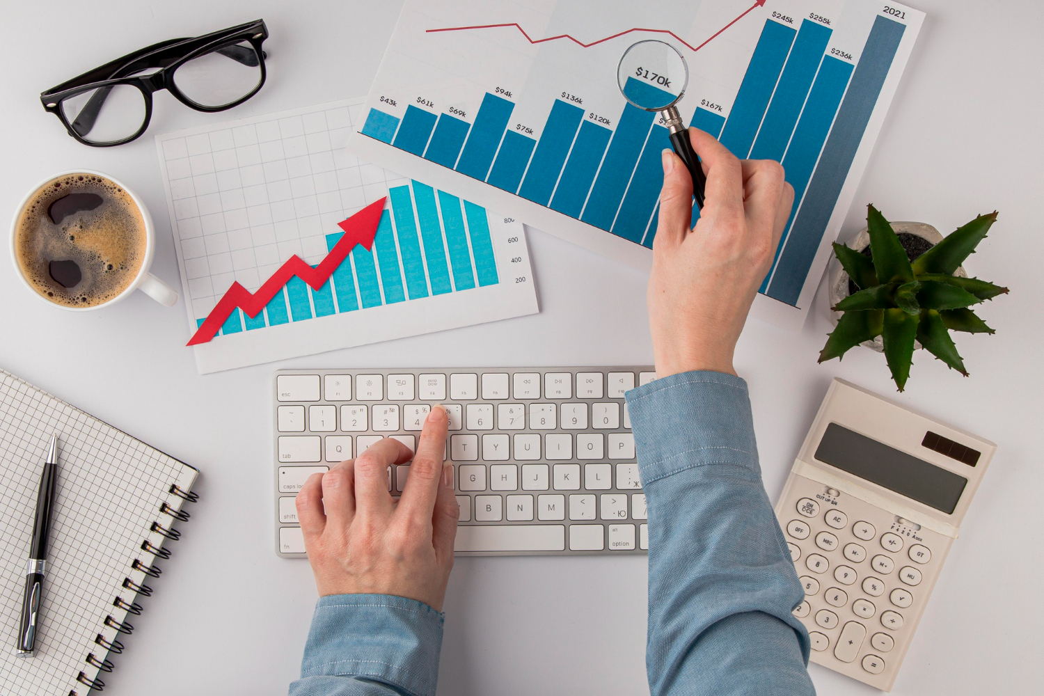 Mãos de um profissional formado em Gestão Financeira EaD, analisando gráficos. Outra mão apoiada em um teclado de computador.